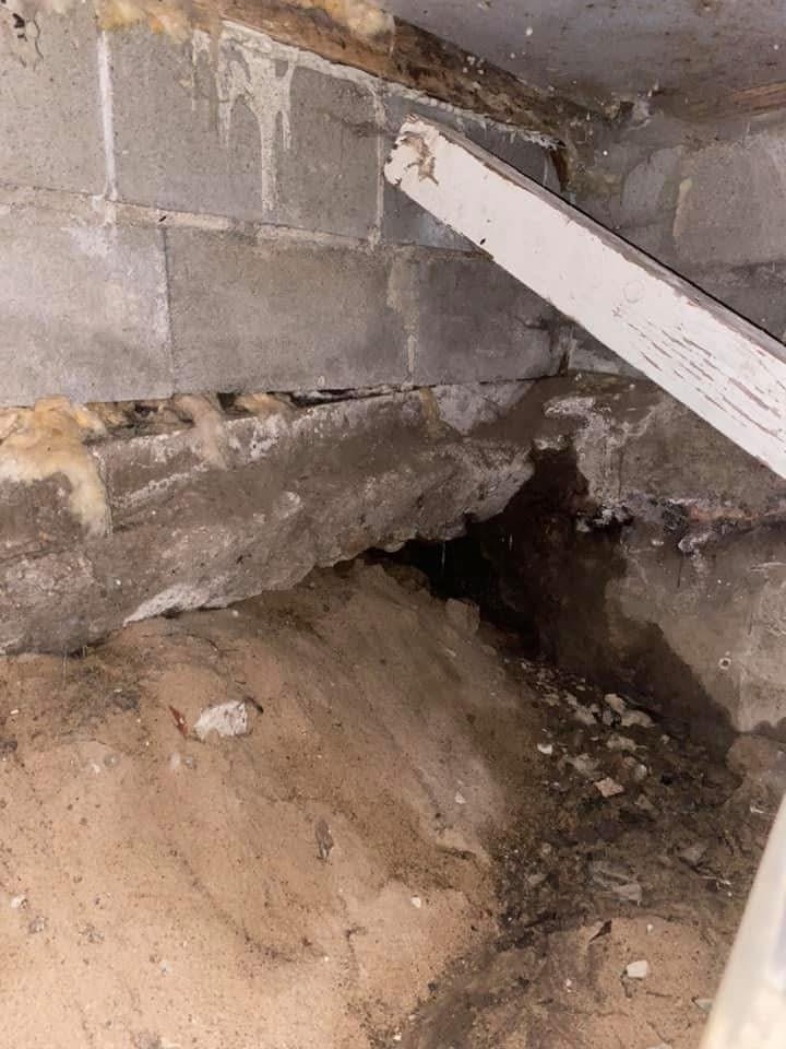 Jagged hole through a crawl space block foundation wall